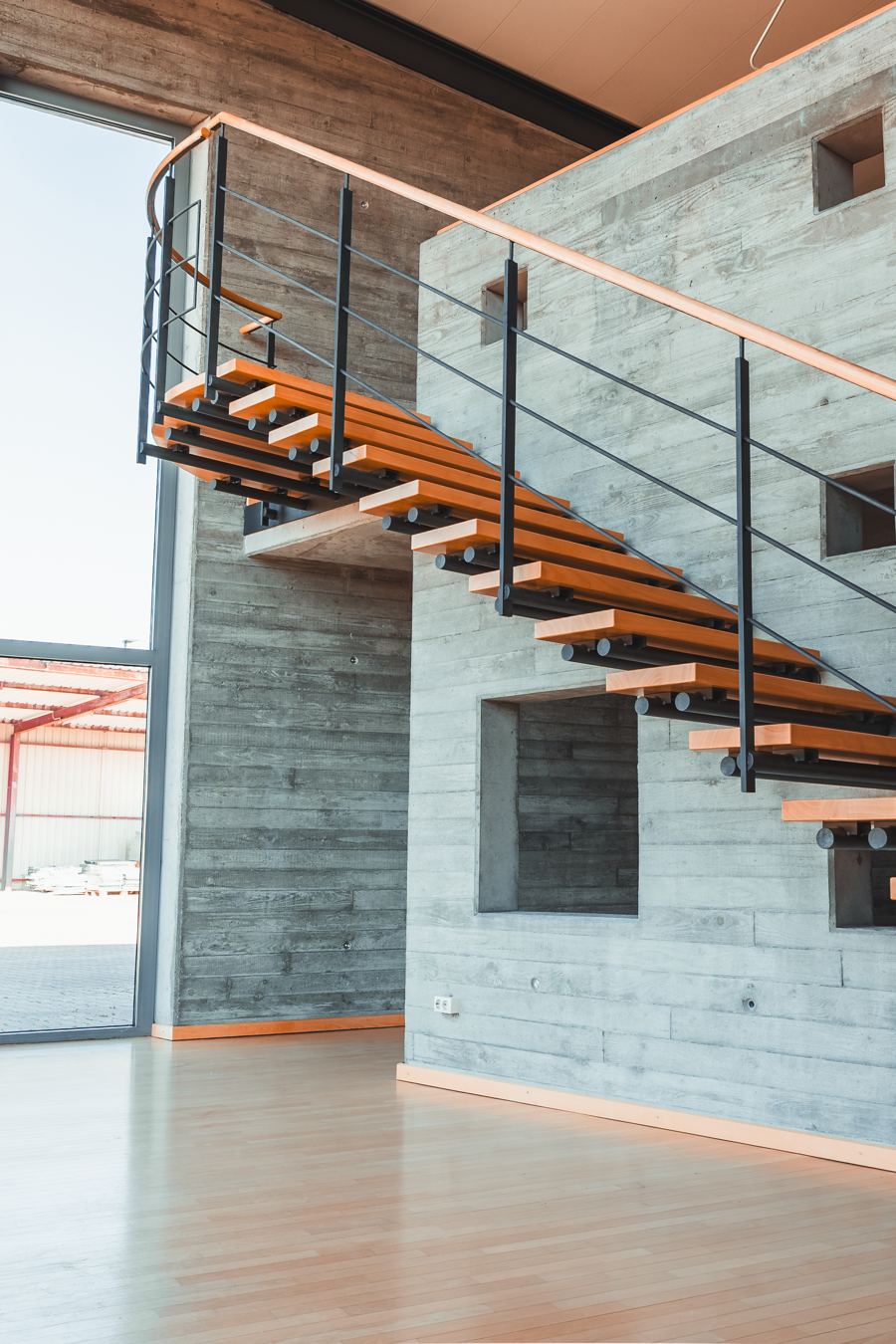 Offene Treppe aus Holz und Stahl vor Sichtbetonwand und Glasfassade
